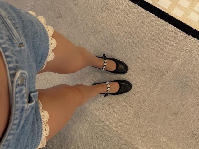 TheHottestBlonde's legs in denim shorts with white lace, wearing black Mary Jane shoes, standing on a gray carpet. Her ass is visible, tan skin. She's wearing no socks.