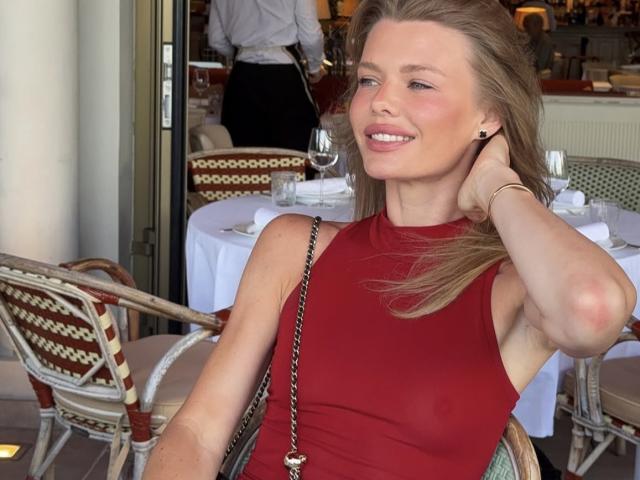 TheHottestBlonde with blonde hair, red sleeveless top, smiling, hand on neck, chain purse, small tits, in restaurant, white tablecloth, wicker chairs, reflection in glass door.