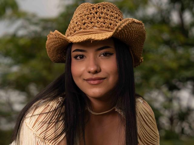 KendallCurves with long dark hair, brown eyes, and tan skin wearing a woven straw hat and fringe top, smiling softly. Boobs not visible, focus on face and hat.
