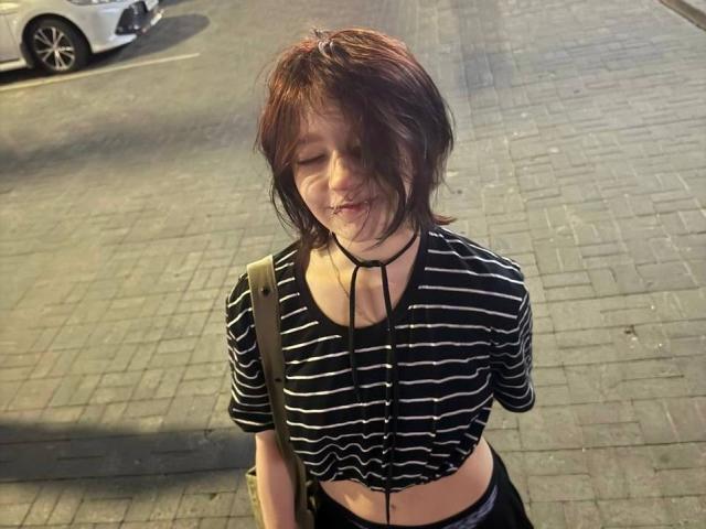Sophia Renlay, con i capelli castano disordinati, una maglietta a righe nere e bianche, una collana nera, sangue sul viso, occhi chiusi, con la bocca semiaperta, indossa pantaloni neri e porta una borsa marrone a tracolla..