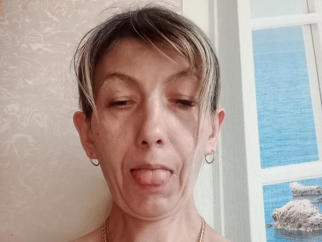 Nerpenok, com cabelo loiro claro e curto, brincos, língua de fora e um leve sorriso. Os olhos de Nerpenok estão semicerrados. O nariz de Nerpenok está levantado, e a pele de Nerpenok é clara..