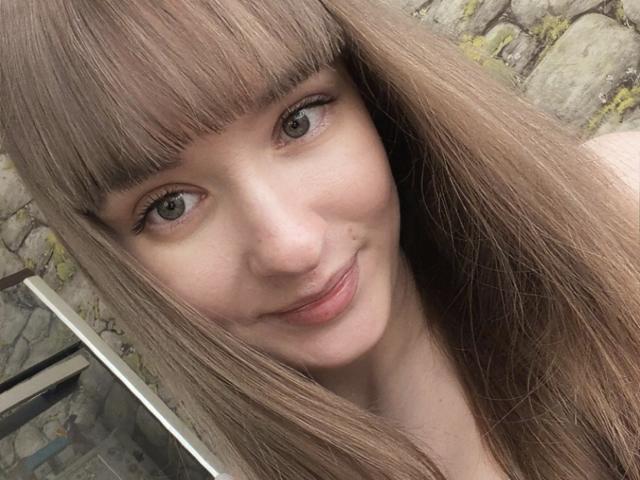 Il selfie di BonnyDee la mostra con lunghi capelli castani lisci, frangia e un sorriso appena accennato. Ha la pelle chiara, occhi castani e una piccola lentiggine sulla guancia destra..
