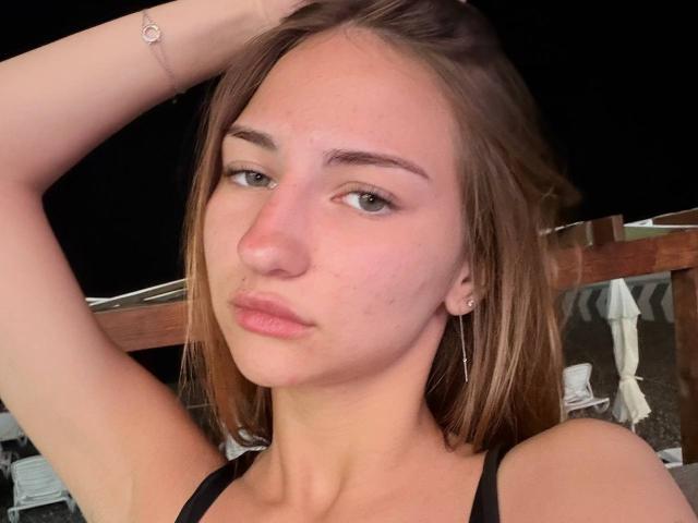 AdrianaNalley tiene un rostro adorable con ojos verde claro, cabello castaño y labios rosados, vestida con una blusa negra, con un brazo levantado, mostrando una pulsera de plata..