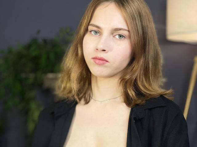 Bethany Aceves a les cheveux bruns clairs, les yeux bleus et une expression neutre. Elle porte une chemise noire avec un décolleté bas, qui révèle ses petites seins. Elle a un collier fin..