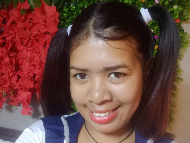 MariahSquirting69 has dark pigtails, brown eyes, and a cute smile with pink lips. She's wearing a blue and white top, and has a small black necklace.