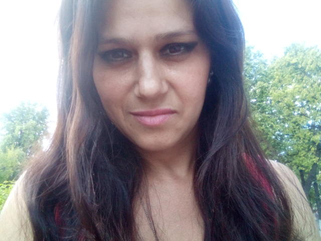 ZinaMillerx heeft lang bruin haar, donkere eyeliner en een lichte frons. Haar lippen zijn roze en gesloten, en ze draagt een top zonder mouwen. Haar borsten zijn niet zichtbaar..