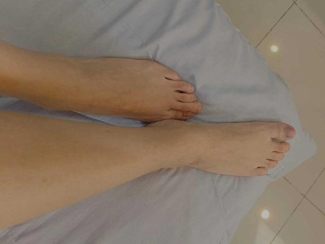 AliCipher's bare feet with slightly dirty toes, lying on a light blue sheet, showing pale skin and small, natural toenails.