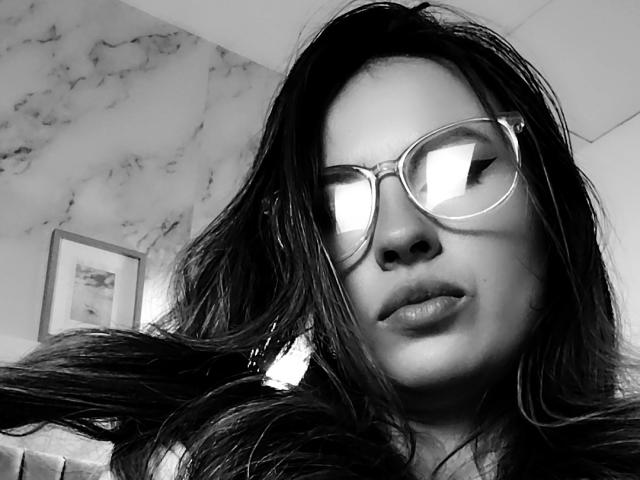 AmiiRosse, con lunghi capelli scuri, che indossa occhiali con lenti riflettenti e labbra piene, in un selfie in bianco e nero. Il suo sedere è leggermente visibile nell'angolo inferiore destro..