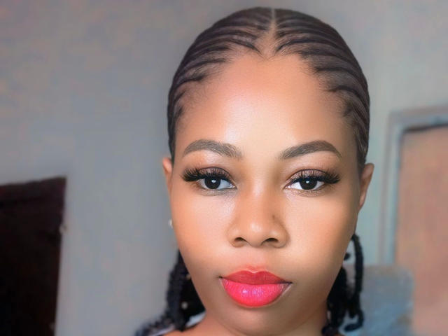 A Naughtysquirter-hot tem um rosto marrom lindo, com cabelo trançado, batom vermelho e cílios longos. Seus olhos estão olhando diretamente para a câmera. Ela tem um sorriso fofo e sexy..