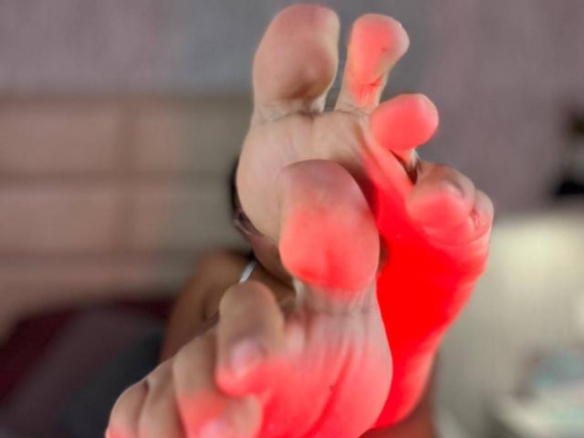 LilithRussoo's red, slightly dirty soles with visible toes and slightly curled pinkish-red edges, foregrounded and blurred. Her feet are the focus, with her face out of focus.