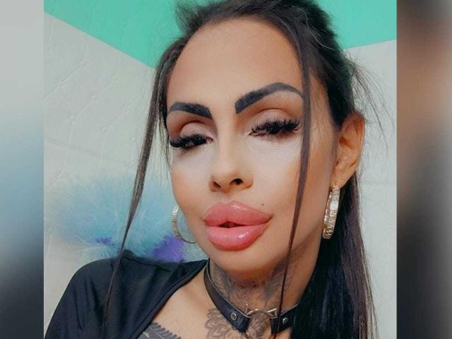 DenyChantal ha labbra piene e rosse, sopracciglia nere e folte, lunghe ciglia e un piccolo tatuaggio sotto il mento. Indossa una collana nera e grandi orecchini scintillanti..