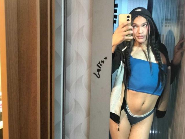 PamelaXFox with long brown hair, blue sports bra, black and white panties, black jacket, and cap, taking a mirror selfie, showing a toned midriff and small ass.