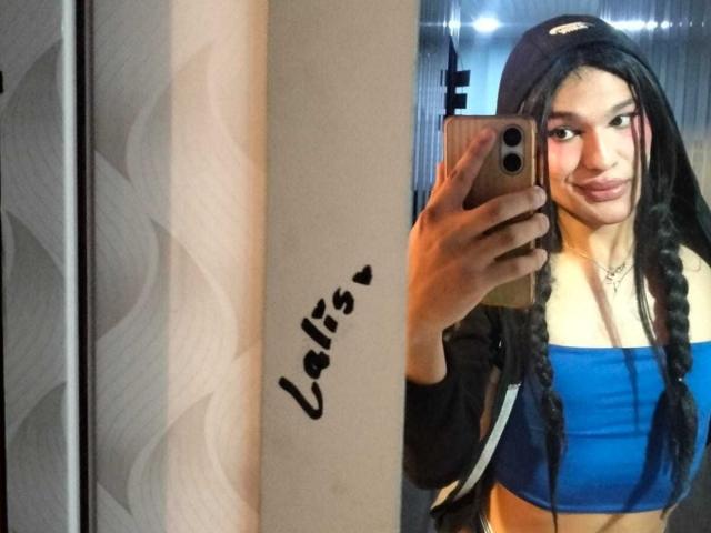 PamelaXFox with long black braids, wearing a black cap and blue tube top, taking a mirror selfie with a confident smile, showing her tits and a cute face.