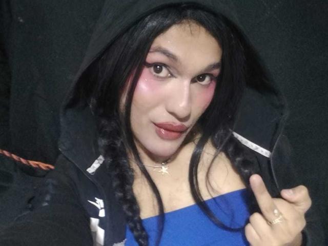PamelaXFox with dark hair in braids, wearing a black hoodie and blue top, has pink eyeshadow, glossy lips, and a star necklace, flashing a middle finger.