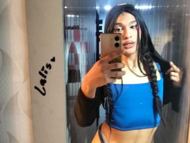 PamelaXFox with long black hair in braids, blue sports bra, black long-sleeve shirt, holding phone, mirror selfie, showing tan skin, slim, small tits, subtle makeup, confident expression.