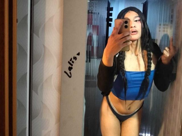 PamelaXFox con lunghi capelli neri intrecciati, un top blu a tubo, biancheria intima nera e maniche nere, che si scatta un selfie allo specchio, mostrando il segno della pace, tenendo un telefono rosa..