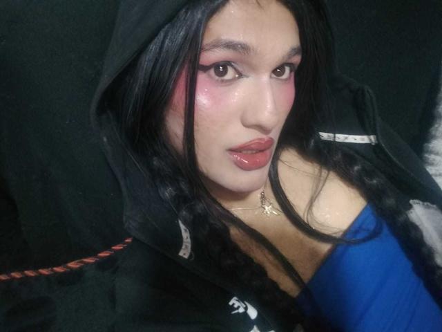 PamelaXFox, con mejillas rosadas brillantes, una sudadera negra y una blusa azul, mostrando labios brillantes y cabello largo y oscuro, lleva un collar dorado. Sus senos son parcialmente visibles..