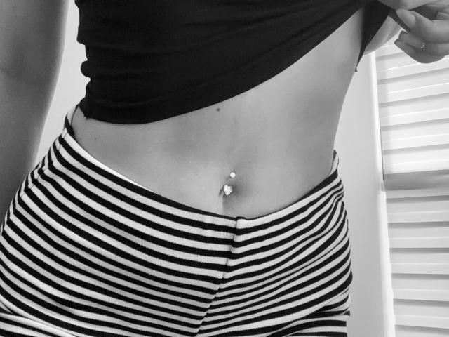 I pantaloni a righe bianche e nere di SugarrX, che mostrano un piercing all'ombelico con due piccole gemme, mentre sollevano una maglietta nera per rivelare il loro addome piatto e tonico..