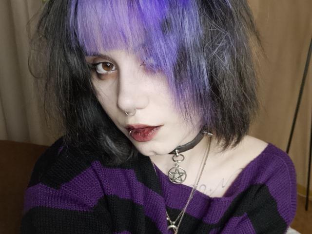 YasukoCella with purple and black hair, brown eyes, nose ring, black choker, pentagram necklace, bloody red lips, black and purple striped shirt, looking at camera.