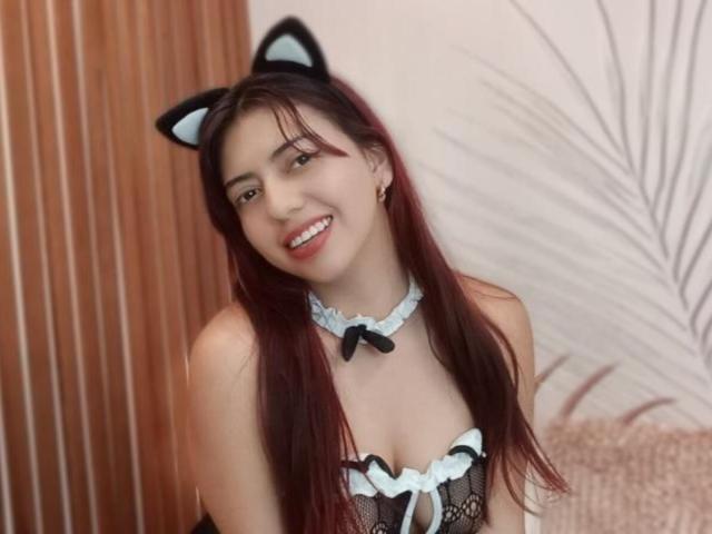 BrendaaPierce with long red hair, cat ears, smiling, wearing black and blue lace lingerie with a ribbon choker, showing her tits. Soft lighting, cute, sexy.