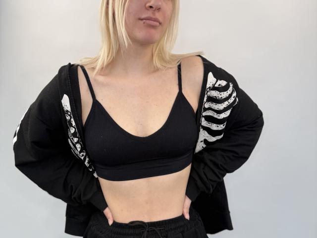 Nancy Ramstad, con i capelli biondi, reggiseno sportivo nero che mette in mostra il seno, e giacca nera con motivi a scheletro bianchi, mani sui fianchi, leggero sorriso, ripresa a mezza figura, posa informale..