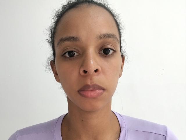 Rachel Willians hat braune Augen, lockiges schwarzes Haar und einen ernsten Gesichtsausdruck. Sie trägt ein lila Hemd, und ihr Gesicht hat einen leichten Glanz. Ihr Hintern ist nicht sichtbar..
