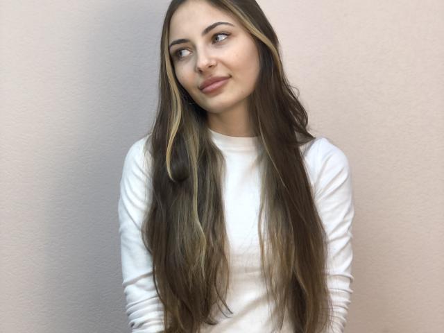 VasilikiMerlette with long brown hair, white long-sleeve shirt, nose ring, and slight smile, looking to the side, with a subtle, sexy, cute, and attractive vibe.