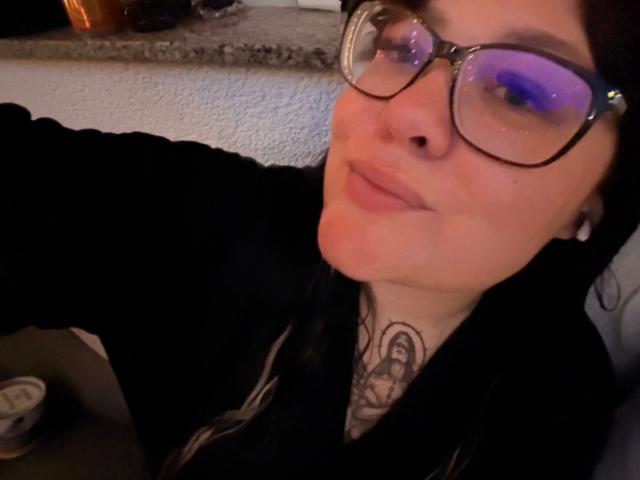 Prettyjosi-hot with glasses, black hoodie, and tattoo on neck, slightly pouty face, and blue reflection in glasses, taking a selfie.