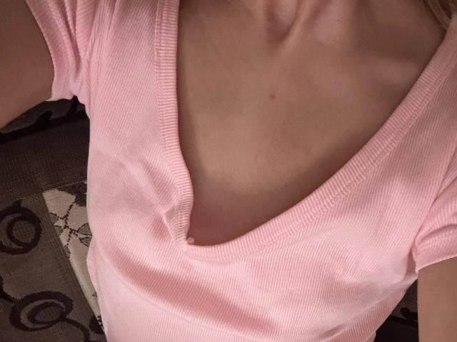 JoetteShigeta's pink ribbed V-neck shirt, showing a slight cleavage and a slender, pale chest. Her arms are partially visible, with a brown patterned surface below.