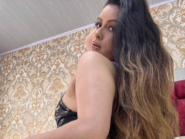 HannaRobertss with long, wavy, brown hair, looking over her shoulder, wearing a black, strapless top, showing her bare shoulder and subtle makeup, with a sultry expression.