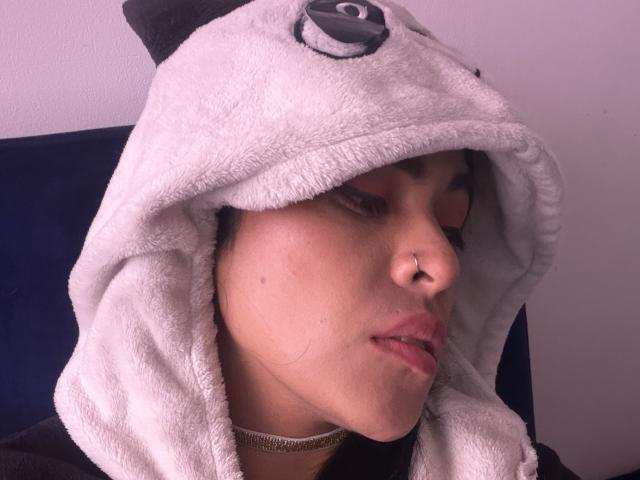 StellaBeckker, con un cappello da panda bianco e soffice che le copre la testa, gli occhi marroni socchiusi, il naso con i piercing, le labbra rosa leggermente dischiuse, indossa una maglietta nera e una collana..