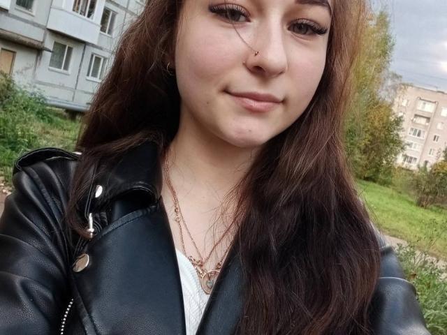 Cherelle Delozier, con lunghi capelli castani, giacca di pelle nera, maglietta bianca e piercing al naso, sorride leggermente, mostrando un piccolo brufolo sulla guancia destra. Il suo seno è piccolo..