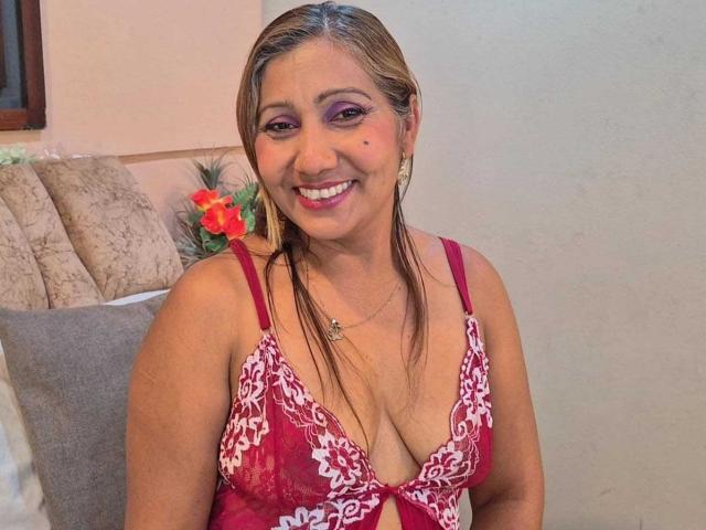 AliciaFerrer with medium tits in a red lace bra, smiling at the camera. She's got pink eyeshadow, brown hair in a ponytail, and a small star necklace.