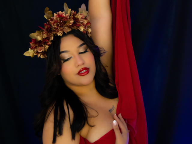 ValeryRiven with red dress, holding fabric, wearing flower crown, eyes closed, red lipstick, black hair, arm raised, small tattoo on chest, dark background, sensual, beautiful.