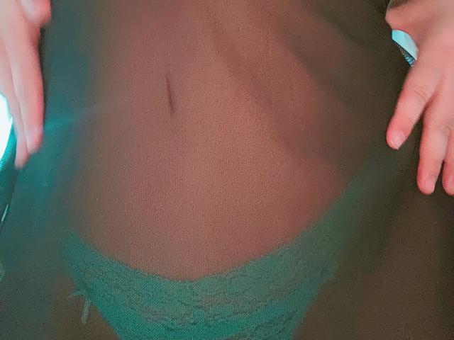 Akkanee's green lace panties are visible through a sheer black fabric, with her hands gently pulling it down, revealing a small, dark navel.