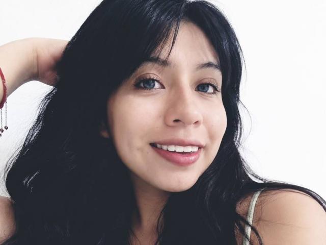 ZoeRedds, con i capelli neri, gli occhi azzurri e un sorriso, indossa un braccialetto rosso, ha un viso carino e sta mostrando i denti. Le sue natiche non sono visibili..