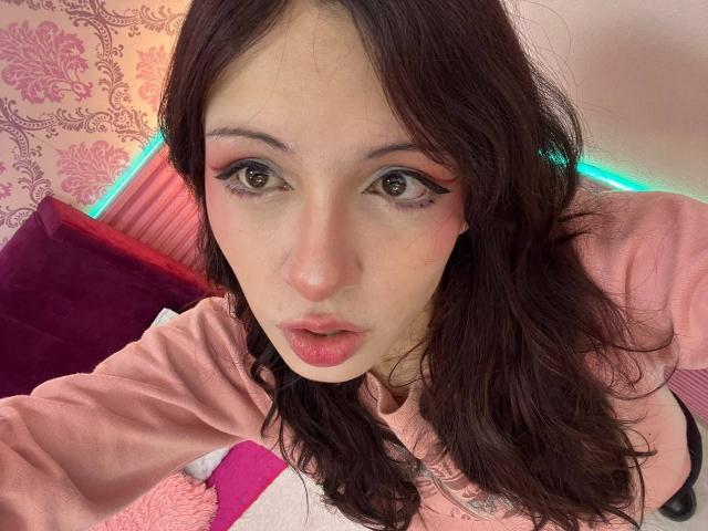 Valery Beaumont tem cabelos castanhos ondulados, sombra rosa nos olhos e lábios entreabertos com uma expressão de surpresa. Ela está vestindo uma camisa rosa, e a foto é um autorretrato..