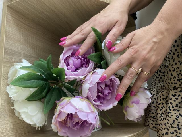 Tilliana's hands with pink nails holding a bouquet of purple and white peonies, wearing a leopard print dress, gold ring, and wooden box.