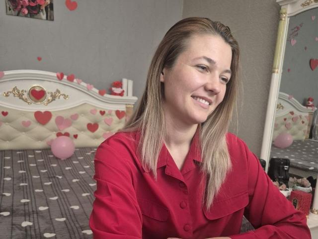 Anshante with medium tits, blonde hair, red button-up shirt, smiling, looking to the side, in a bedroom with heart decorations and balloons.