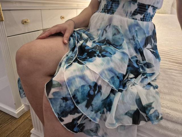Anshante's skirt is lifted, showing her pale thigh. She's wearing a blue and white floral dress, with her hand on her thigh. Her dress has a ruffled, layered design.
