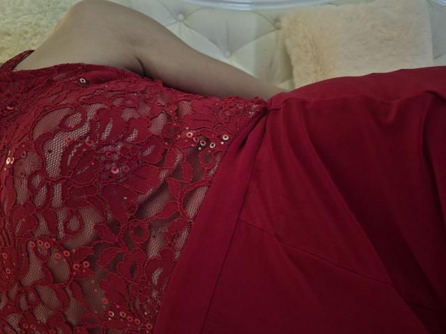 Anshante's red lace dress with sequins, showing her tits, lying on a white bed with a beige pillow. Her arm is partially visible.