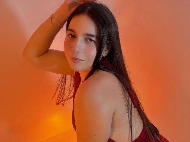 Valentina Riva, met lang donker haar, een rode haltertop, kijkt over haar schouder, met een arm omhoog, oranje verlichting, een subtiele glimlach, lichte huid, kleine oorbellen, slank postuur, klein achterwerk, zachte huid..