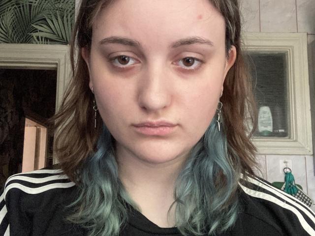 Johnette Perrotta ha i capelli ondulati tinti di blu, occhi marroni e un'espressione neutra. Indossa una camicia a righe nere e bianche e piccoli orecchini. Il suo viso presenta alcune piccole imperfezioni..