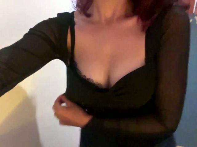 ElbaHuppenbauer, con i capelli rossi, indossa una maglia nera trasparente che mette in mostra il seno, con una mano sulla vita, in un'immagine leggermente sfocata..