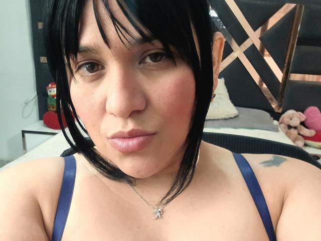 VivianaThompson has short black hair, light skin, and is wearing a blue spaghetti strap top with a silver necklace. She has a tattoo on her right shoulder.