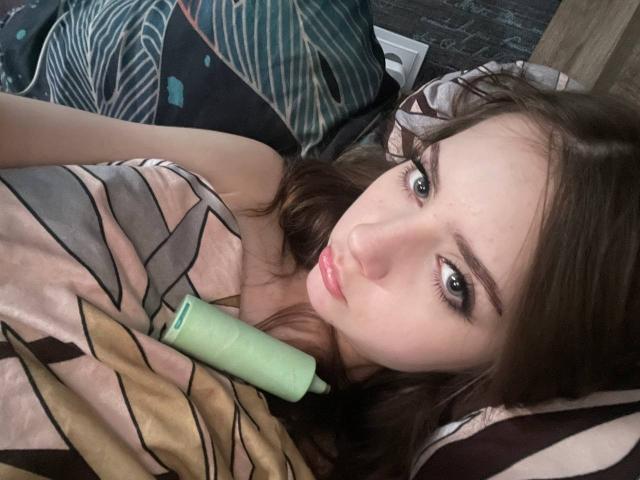 MorganCastellanoz tiene ojos verdes, piel clara y cabello castaño, y está acostada en la cama con una manta de color rosa y negro, y un vibrador verde cerca de sus senos..