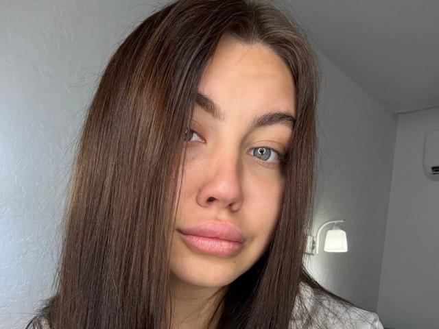 InesGueningsman has long brown hair, blue eyes, and pink lips. She's looking slightly to the side with a neutral expression. Her nose is small and she has thin eyebrows.