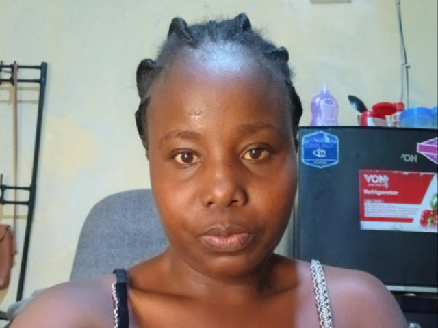 StellaAileen has dark brown skin, small breasts, and short braided hair. She's wearing a black and white spaghetti strap top, looking serious with a slight pout.