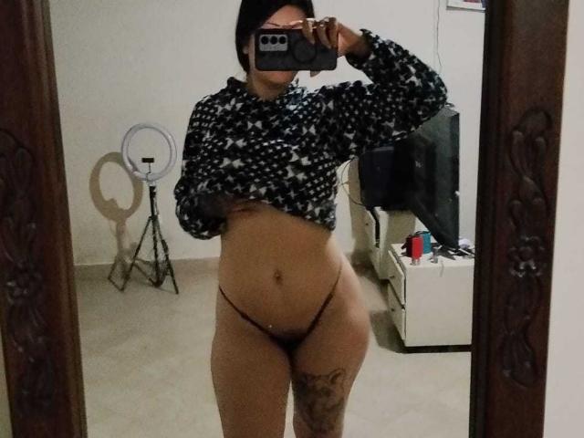 Helena Morningstar macht ein Selfie vor einem Spiegel und trägt einen schwarzen Hoodie mit Sternenmuster. Sie hebt ihn an, um ihre Brüste zu zeigen, und trägt einen braunen String, der ihr Gesäß und ein Tattoo an ihrem Oberschenkel zeigt..