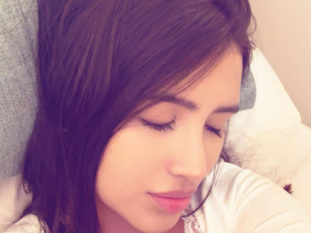 AnnaPooky's face, with closed eyes and dark brown hair, shows a soft smile. Her eyelashes are long and she's wearing pink lipstick. She's wearing a white shirt.